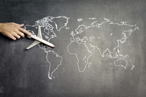 From above of crop anonymous person driving toy airplane on empty world map drawn on blackboard representing travel concept