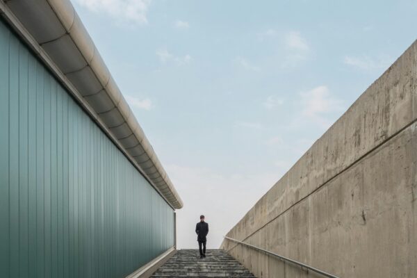 A solitary person walking down marble stairs between modern buildings under clear skies.