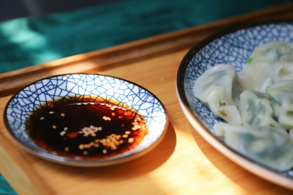 A close-up of delicious homemade dumplings with soy sauce in cracked blue ceramic bowls on a wooden tray.