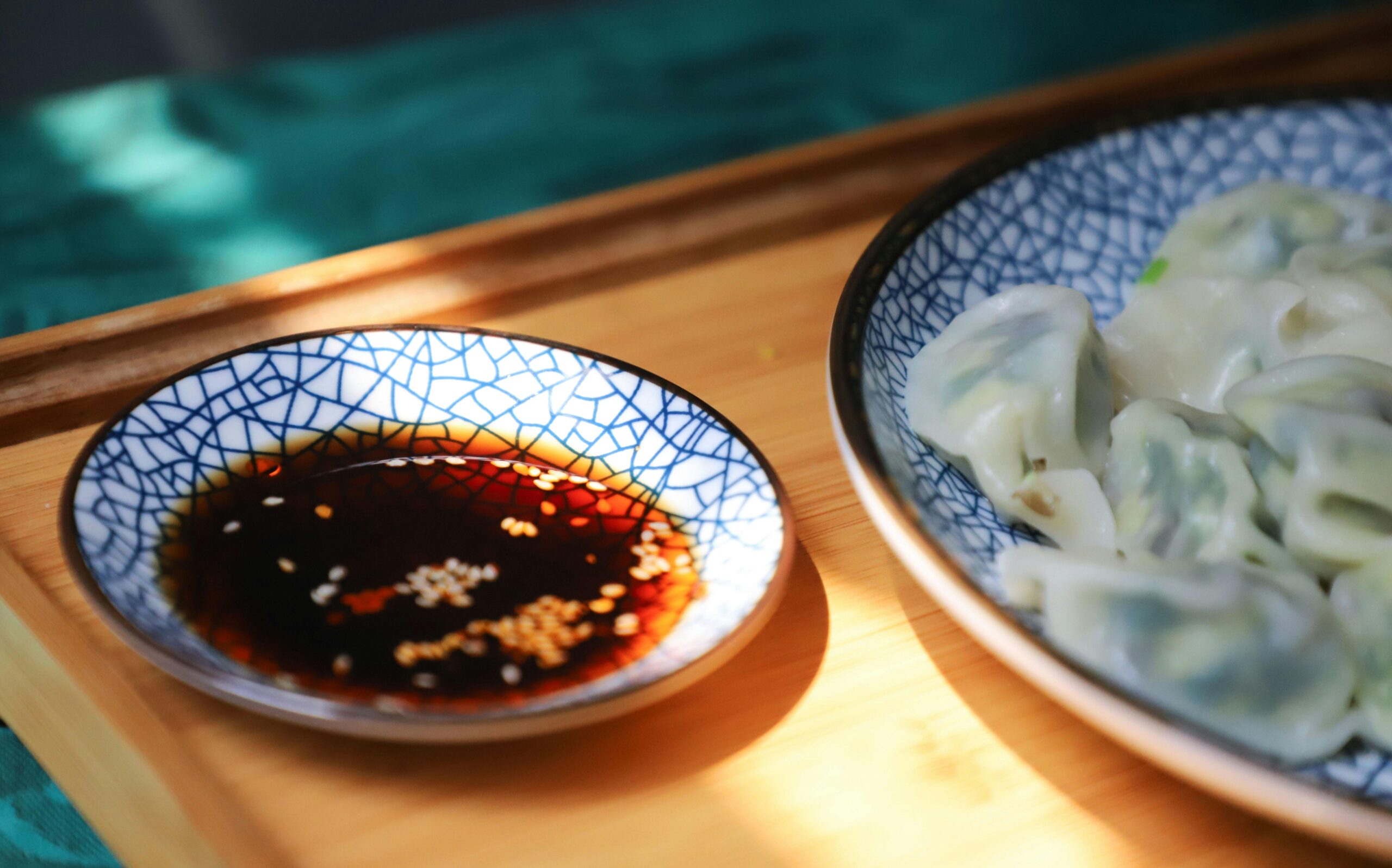 A close-up of delicious homemade dumplings with soy sauce in cracked blue ceramic bowls on a wooden tray.