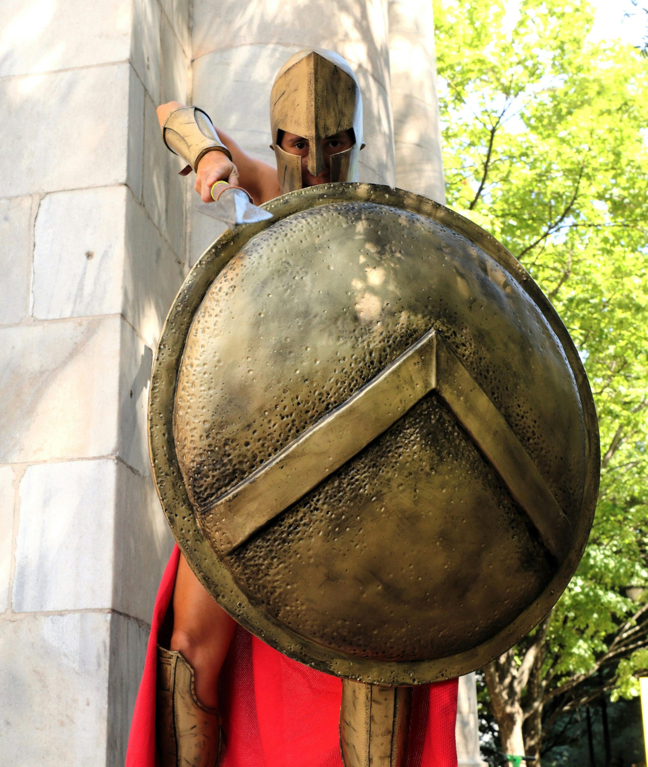A Spartan warrior in armor holding a shield outdoors on a sunny day.
