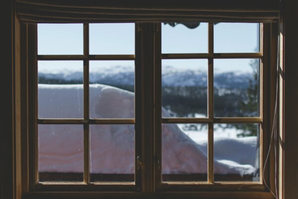 A scenic view of snow-capped mountains through a wooden window frame, capturing the serene winter landscape.