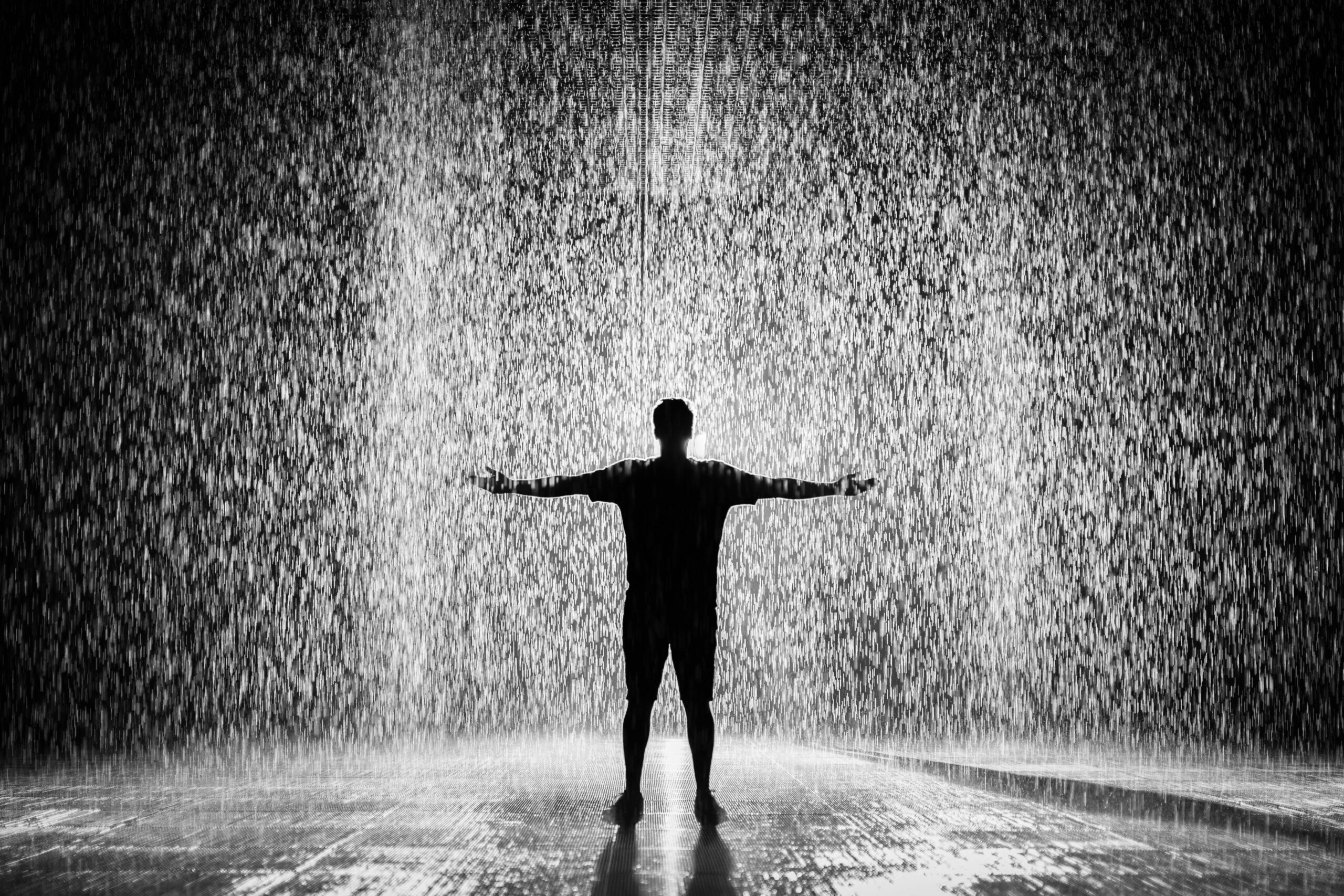 A person joyfully standing in the rain with arms wide open in a dramatic black and white scene.