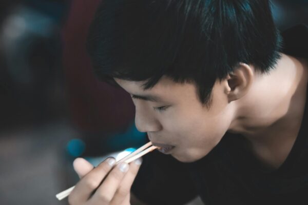 A young man savoring a tasty meal with chopsticks in an indoor setting, enjoying the moment happily.