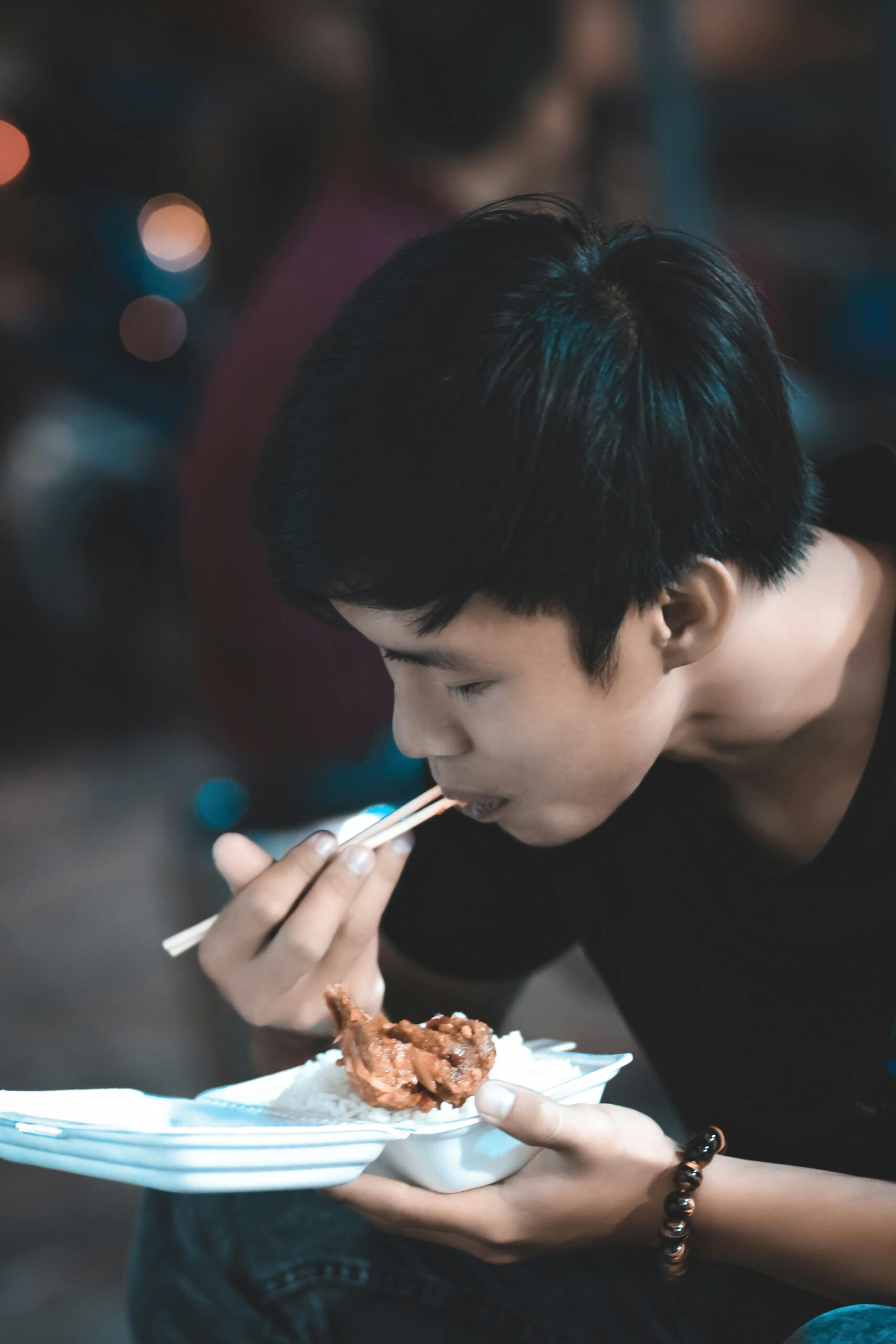 A young man savoring a tasty meal with chopsticks in an indoor setting, enjoying the moment happily.