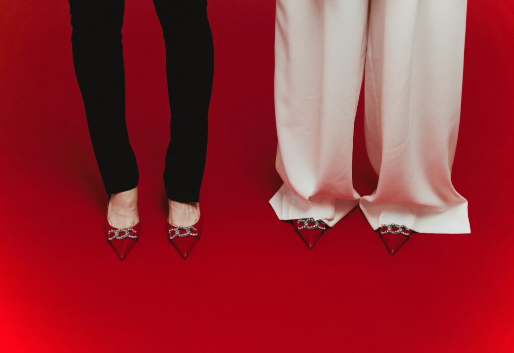 Elegant red shoes with crystal designs paired with black and white pants on red surface.