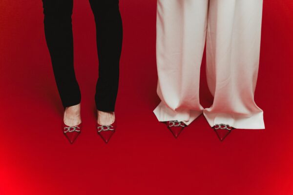 Elegant red shoes with crystal designs paired with black and white pants on red surface.